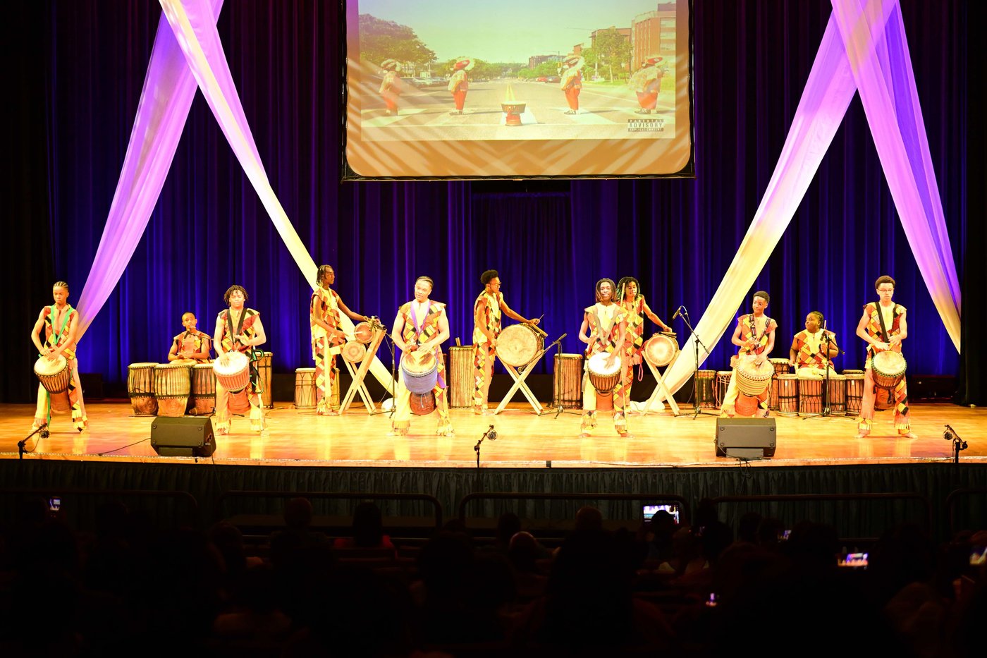 Drummers lined up across the UDC stage at Birthright, lit in blue and purple