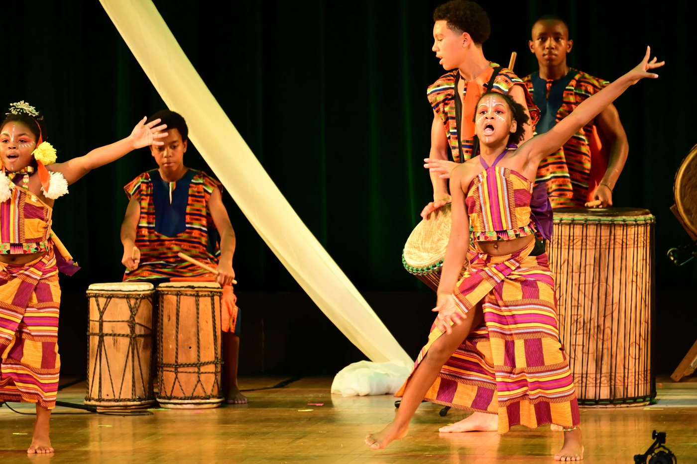 Young performers in face paint and orange dress mid-performance at Birthright