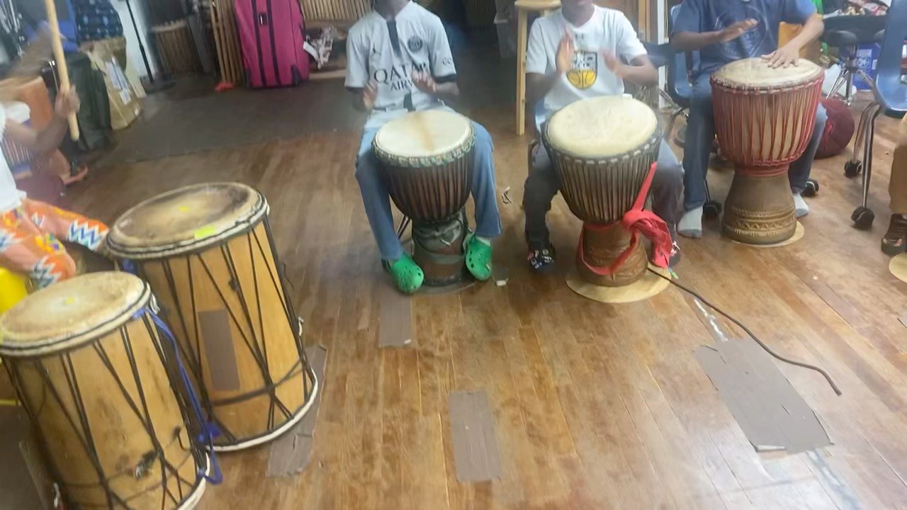 Three boys playing djembes in a row during class, close on their hands
