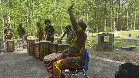 An instructor leading a children's drum class outdoors in a park