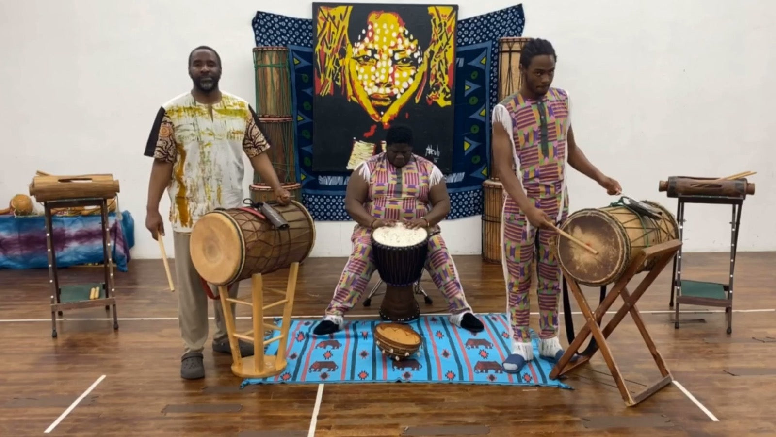Mahiri Fadjimba Keita leading a drum ensemble in the studio, flanked by two students playing dunun